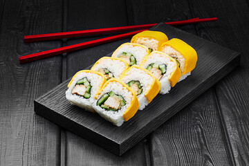 Japanese rolls, rice sushi with melted cheese, cucumber and chicken on a black wooden background.