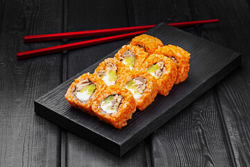 Japanese rolls, sushi made of rice in red sauce with tuna, cucumber and cheese on a black wooden background.