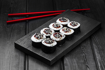 Japanese rolls, rice sushi with teriyaki sauce and sesame on black wooden background.