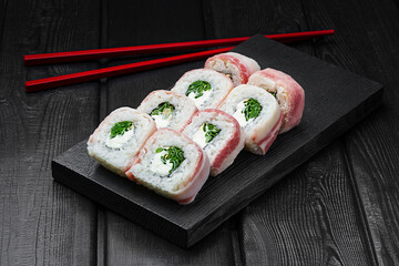 Japanese rolls, sushi with bacon, green onions and cream cheese on black wooden background.