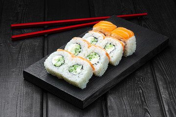 Japanese rolls, Philadelphia sushi with salmon, cucumber and cheese on a black wooden background.