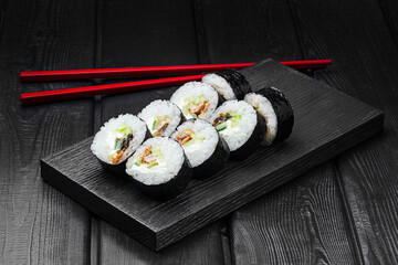 Japanese rolls, sushi with eel, cucumber and cheese on a black wooden background.