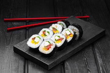 Japanese rolls, sushi with chicken, pepper, tomato, cucumber and cheese on a black wooden background.