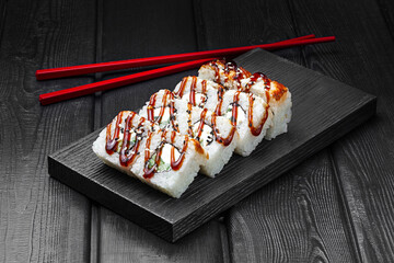 Japanese rolls, rice sushi with teriyaki sauce, cucumber and cheese on a black wooden background.