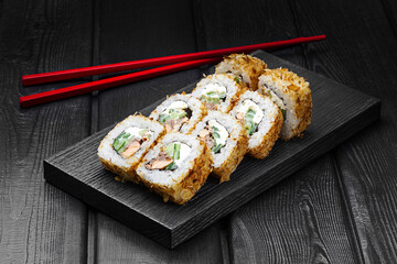 Japanese rolls, sushi with canned tuna, cucumber and cream cheese on black wooden background.