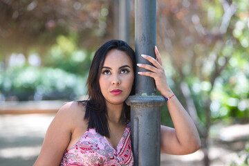 brunette, young and beautiful woman holds an iron lamppost with one hand and puts her face next to...