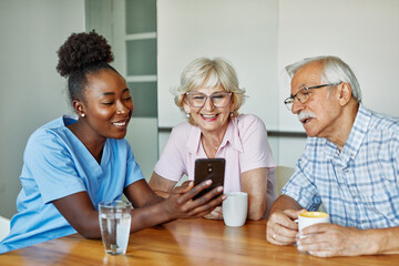 nurse senior couple home care mobile phone  smartphone patient elderly retirement caregiver assistance nursing showing screen laughing using