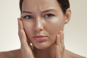 Close-up of a woman with clear skin touching her face, showing a concerned expression, highlighting...