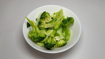 Cooked broccoli in a white bowl on a white background