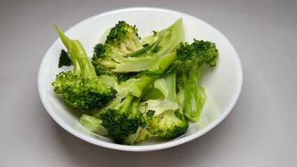 Cooked broccoli in a white bowl on a grey background, close up