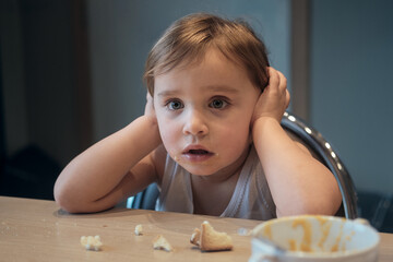 frustrated toddler covering ears during mealtime, expressing overwhelm childhood emotions