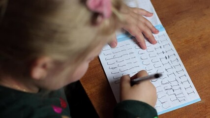 The child learns to write at home, draws a letter. The girl circles the letters along the line, writes for the first time. A preschooler learns to write at the table