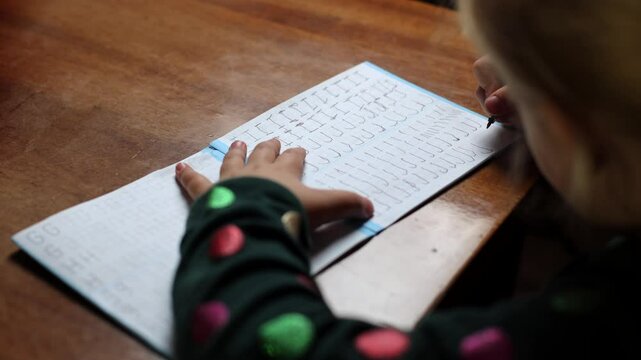 The child learns to write at home, draws a letter. The girl circles the letters along the line, writes for the first time. A preschooler learns to write at the table