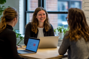 Female manager smiling while talking to two people in an office. One of them is sitting at the table with a laptop.