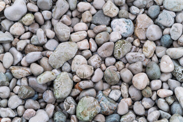 A collection of smooth, rounded pebbles and stones in various shades of grey, beige, and light green. The pebbles are of different sizes and shapes, creating a natural, textured surface. 