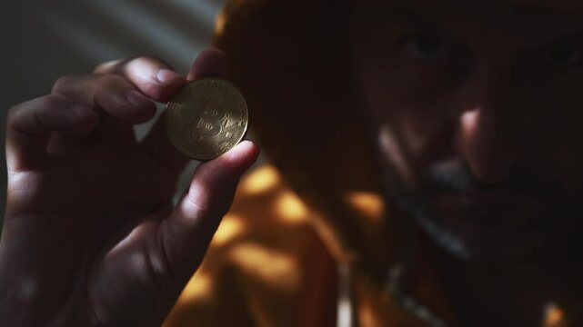 Computer hacker and cryptocurrency scammer in golden yellow hooded jacket holding Bitcoin in hand, 4K