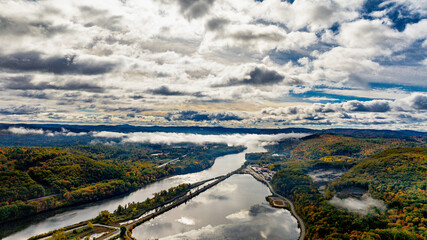 Aerial view of a serene river landscape in autumn. The landscape captures a tranquil river surrounded by colorful autumn foliage and dramatic cloudy skies in the USA.