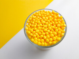 Yellow masterbatch granules in shot glass on yellow and white background,color pigment carrier...