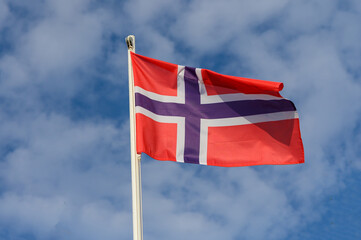The vibrant Norwegian flag billowing against a backdrop of soft clouds on a bright sunny day in Norway