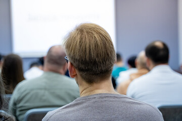 A man is currently sitting in a classroom environment attentively watching a presentation being...