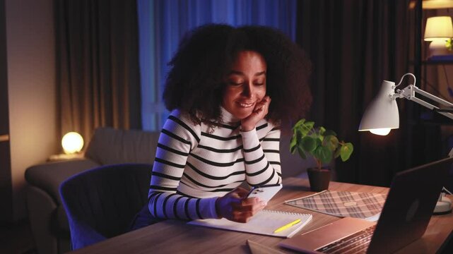 Positive young african american woman student relaxing at home take a break from study typing browsing products in internet online store reading news or social media profile on smartphone at night