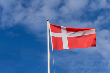 A vibrant Danish flag billows against a bright blue sky, symbolizing national pride and history in Denmark during a sunny day