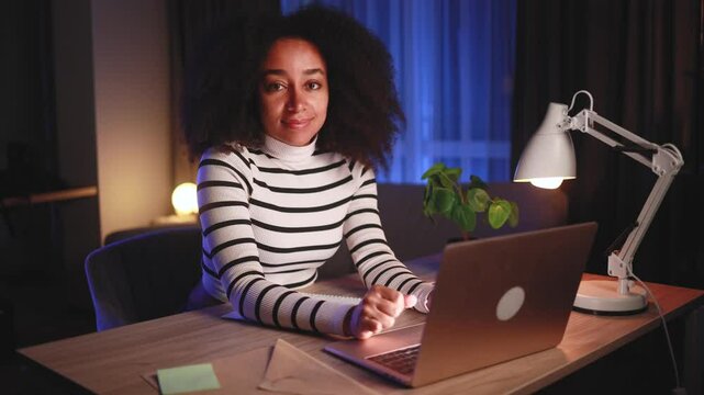 Pretty young woman freelancer or student looking at laptop screen with nod of approval at home workplace looking at camera and show thumbs up at night indoors Advise Approve Recommend Choice concept