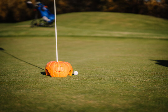 A carved pumpkin with a golf flag and ball on a green, combining Halloween decorations with a golf theme..