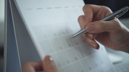 Closeup, woman hand writing on calendar event planner to set timetable organize schedule, event...