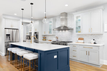 A kitchen with blue and grey cabinets, a large island with gold and white bar stools sitting at the...