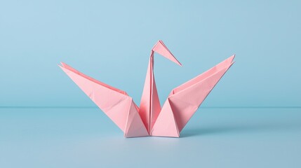Fototapeta premium A delicate pink origami crane gracefully stands against a soft blue background, showcasing the art of paper folding.