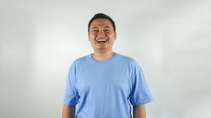 A young Indonesian man wearing a blue t-shirt is laughing facing forward