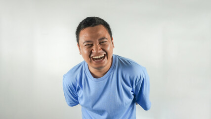 A young Indonesian man wearing a blue t-shirt is laughing facing forward
