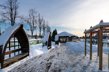 Beautiful winter landscape in the rays of the evening sun. A recreation area with .benches and a gazebo on the private territory of a country village.
