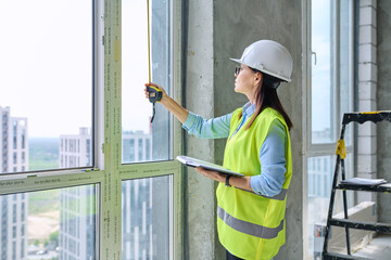 Woman in safety vest hard hat with tape measure on new residential or commercial real estate site