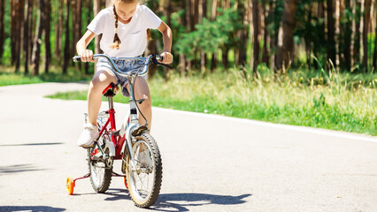 Fototapeta premium Child riding a bike in summer park. Children learning to drive a bicycle on a driveway outside. Kid riding bike. Child on bicycle, bike outdoor.