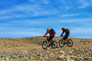 Fototapeta premium Two cyclists riding bikes on a rocky mountain trail.