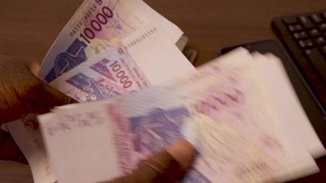Closeup shot of black African hands counting 10000 West African cfa franc notes