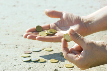 A man counts his change after cash purchases in Europe, close-up photo. Male hands holding coins of different denominations against the background of metal money scattered on the surface.