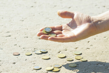 A man holds out his hand with change, holding it over the metal coins lying on the surface in denominations of 2 and 1 euro, as well as 50, 20, 10 and 5 euro cents. The concept of poverty in Europe.