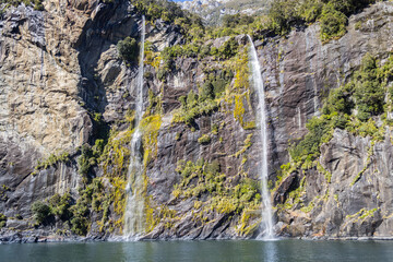 Waterfall cascading down rocky cliff in milford sound fiordland new zealand