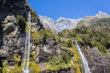 Waterfall cascading down rocky cliff in milford sound fiordland new zealand