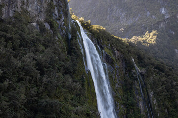 Waterfall cascading down mountain into milford sound, new zealand