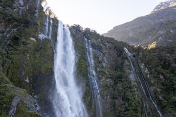 Waterfall cascading down mountain into milford sound, new zealand