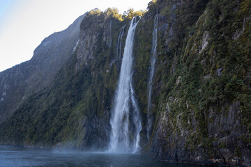 Waterfall cascading down mountain into milford sound, new zealand