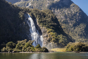 Waterfall cascading down mountain into milford sound, new zealand