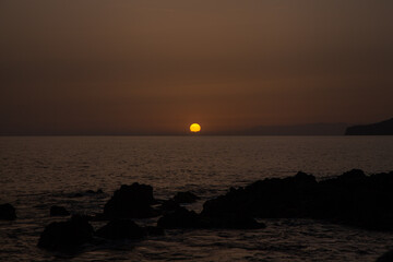 Sun setting over calm ocean water with silhouetted coastline