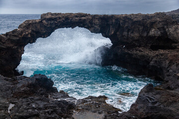 Fototapeta premium Volcanic natural arch forming a bridge over the ocean with a cloudy sky