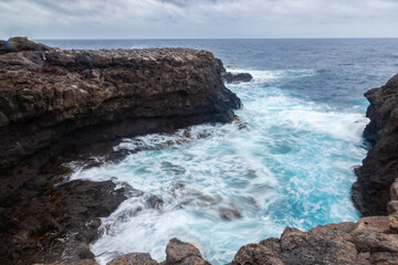 Ocean waves crashing on volcanic rocks at the foot of a cliff