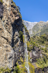Waterfall cascading down rocky cliff in milford sound fiordland new zealand